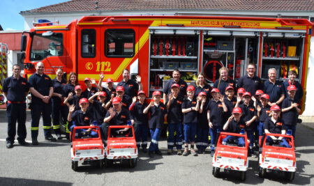 Große und kleine Feuerwehrmänner und -frauen sowie Einsatzfahrzeuge, in Reihe aufgestellt bei einem monatlichen Treffen der Kinderfeuerwehr in Strempt. Foto: Henri Grüger/pp/Agentur ProfiPress