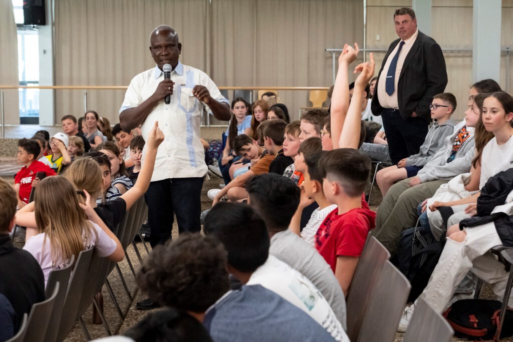 Zahlreiche Finger hoch: Die Schülerinnen und Schüler der Euskirchener Marienschule hatten etliche Fragen an die afrikanischen Gäste um Cesar Beogo. Auch Schulleiter Michael Mombaur hörte interessiert zu. Foto: Ronald Larmann/pp/Agentur ProfiPress