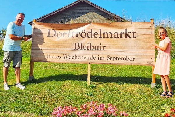 André Neubauer und Tochter Leonie am großflächigen Plakat gegenüber der Bleibuirer Pfarrkirche St. Agnes. Auch an der B 266 am Abzweig Hergarten/Mülldeponie wurde ein Hinweis aufgestellt. Foto: Jutta Neubauer/pp/Agentur ProfiPress