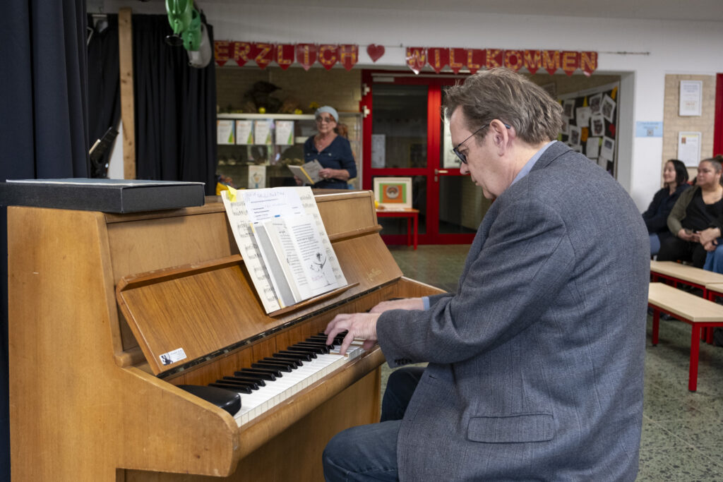 Pianist Manfred Schümer begleitet die Lesung musikalisch. Im Hintergrund zu sehen Sozialpädagogin Gerlinde Suetake, die die Leseclub-Kids bei der Aktion unterstützte. Foto: Ronald Larmann/pp/Agentur ProfiPress