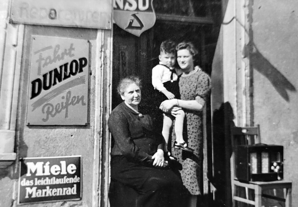 „Vater Ernst hat nie die Übersicht verloren und immer die Ruhe behalten“: Der kleine Günther Schulz auf dem Arm von Tante Mie und mit Oma Auguste vor dem allerersten Geschäft von Zweirad Schulz in Lengwethen, 25 Kilometer südlich von Tilsit/ Ostpreußen. Repro: Manfred Lang/pp/Agentur ProfiPress 