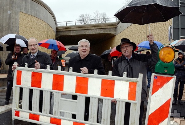 Bürgermeister Dr. Hans-Peter Schick (v.l.), Straßenbaufunktionär Edgar Klein und Vize-Bürgermeister Peter Wassong räumen die letzte Bake beiseite und geben damit den Verkehr durch die Bahnunterführung der B 477 am Mechernicher Bahnhofsberg für den Verkehr frei. Foto: Steffi Tucholke/pp/Agentur ProfiPress