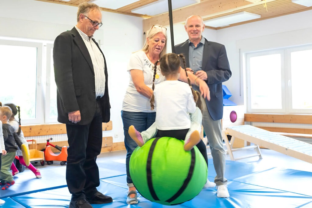 Kinder fliegen durch die Luft angeschubst von Kita-Leiterin Beate Hausmann-Solh. Ralf Claßen (r.) und Dr. Michael Stöhr freuen sich, dass mit der Spende der Mechernich-Stiftung der Schaukelball angeschafft wurde. Foto: Larmann/pp/Agentur ProfiPress