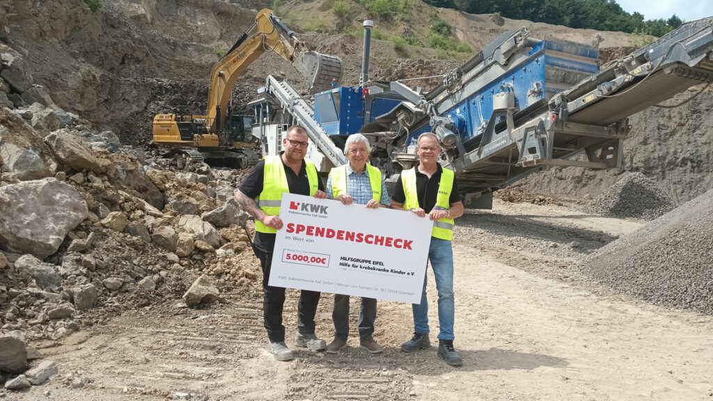 Mit schwerem Gerät im Steinbruch in Rinnen übergaben Betriebsleiter Oliver Nuß (l.) und KWK-Geschäftsführer André Raser ihren symbolischen Spendenscheck an Hilfsgruppen-Chef Willi Greuel (m.). Foto: Reiner Züll/ pp/Agentur ProfiPress
