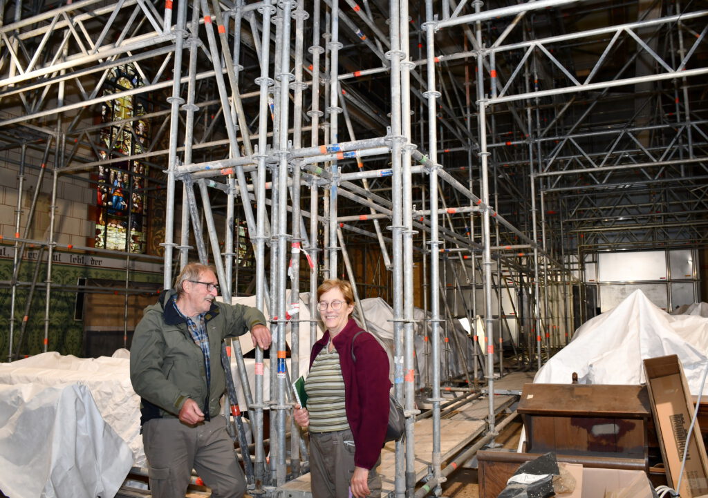 Komplett eingerüstet ist die Pfarrkirche St. Lambertus in Holzheim innen und außen. Helga Leinenbach, die stellvertretende Kirchenvorstandsvorsitzende, und Kirchenvorstand Jochen Emonds berichten vor Ort, dass die Gottesdienste seit Weihnachten 2022 im benachbarten Pfarrheim gefeiert werden. Foto: Manfred Lang/pp/Agentur ProfiPress
