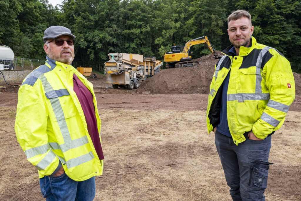 Im Hintergrund die „überdimensionierte Betonmaschine“, die beim Damm-Bau in Vussem zum Einsatz kommt. Andreas König, Projektleiter der Stadt Mechernich, und Marco Müller von Baustark Müller verantworten die Baustelle. Foto: Ronald Larmann/pp/Agentur ProfiPress