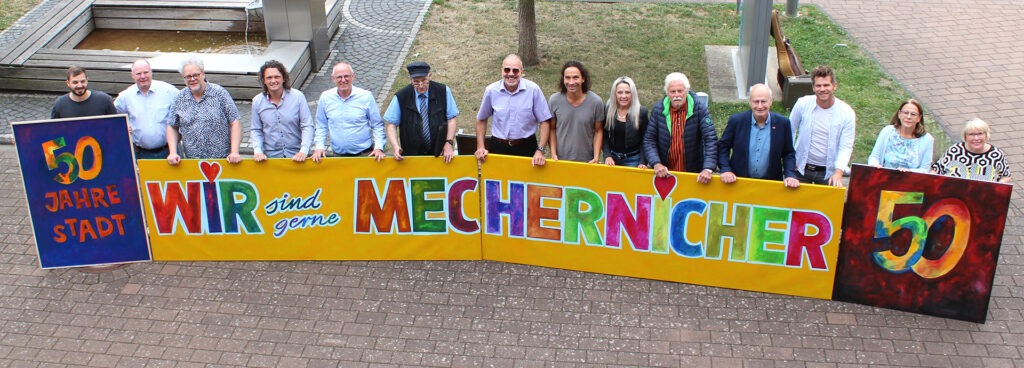 Viel Lust auf ein großes, fröhliches Stadtfest macht das knallbunte, vom Mechernicher Kurator Franz Kruse entworfene Kunstwerk, das die Musiker und Verantwortlichen nun vor dem Rathaus präsentierten. Foto: Kerstin Rottland/pp/Agentur ProfiPress