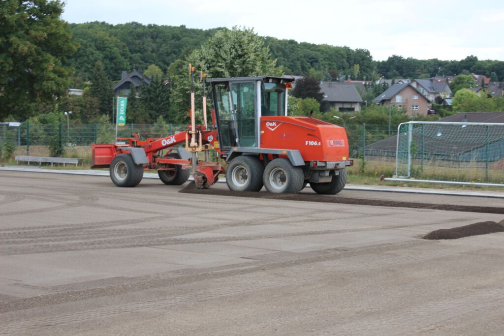 Mit dem Grader wird aktuell eine feine Lavaschicht eingeebnet. Auf sie kommt die elastische Tragschicht, die den Kunstrasen hält. Damit er nicht verrutscht, werden pro Quadratmeter 25 Kilogramm Sand verteilt. Foto: Kerstin Rottland/pp/Agentur ProfiPress