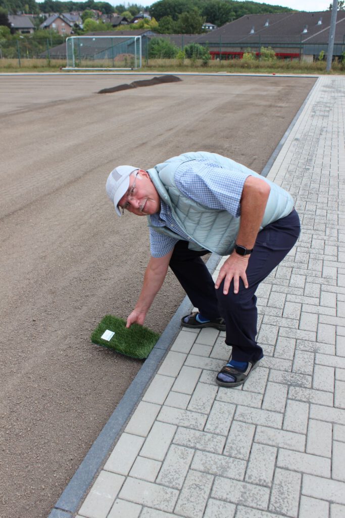 „Hier kommt er hin!“ Diplom-Ingenieur Christof Marx zeigt, wie es einmal aussehen wird, wenn das künstliche Grün namens „Ultra 360“ in der Farbe „Fieldgreen/Olive“ verlegt ist. Foto: Kerstin Rottland/pp/Agentur ProfiPress