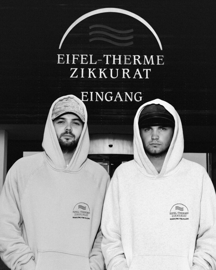 Mode, die international für Aufsehen sorgt, und in der ganz viel Mechernich steckt, macht Designer Luis Dobbelgarten (r.). Hier zeigt er mit seinem Bruder und Manager Leon Dobbelgarten den Hoodie mit Eifel-Therme-Zikkurat-Emblem. Foto: No/Faith Studios/pp/Agentur ProfiPress 