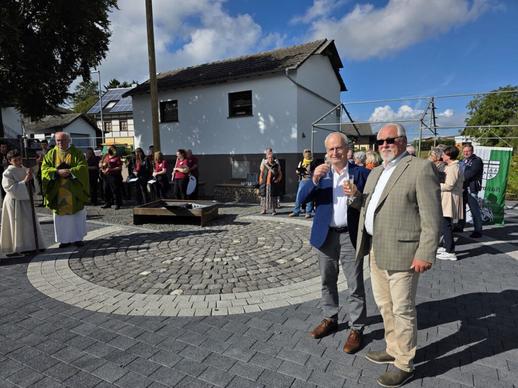 Sonnenschein und strahlende Gesichter bei Bürgermeister Hans-Peter Schick, Ortsbürgermeister Robert Ohlerth und den Kallmutherinnen und Kallmuthern, die nach der Einweihung durch Pfarrer Erik Pühringer auf ihren neuen Dorfplatz anstießen. Foto: Privat/pp/Agentur ProfiPress