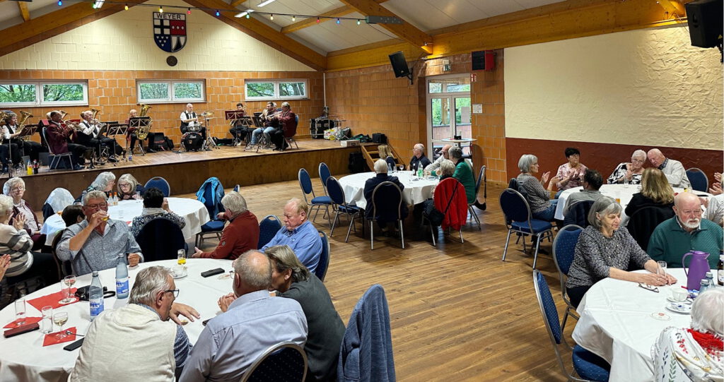 Bei Kaffee, Kuchen und Musik: Zahlreiche Seniorinnen und Senioren genossen den gemütlichen Nachmittag in der Weyerer Bürgerhalle. Im Hintergrund sorgt der Musikverein „Harmonie Weyer“ mit Blasmusik für gute Stimmung. Foto: Mathias Hansen/pp/Agentur ProfiPress