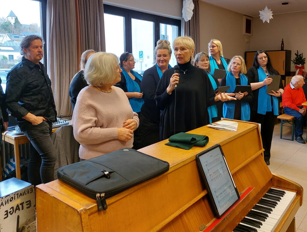 Ursula Koch (m.), die Vorsitzende des Kirchenchores Mechernich und Moderatorin des „Hüttenzaubers“ interview Gabriele Möbius von der Indienhilfe Köln inmitten von Sängerinnen und Sängern des von Pascal Lucke geleiteten Chores „Lumora“. Foto: Agnes Peters/pp/Agentur ProfiPress