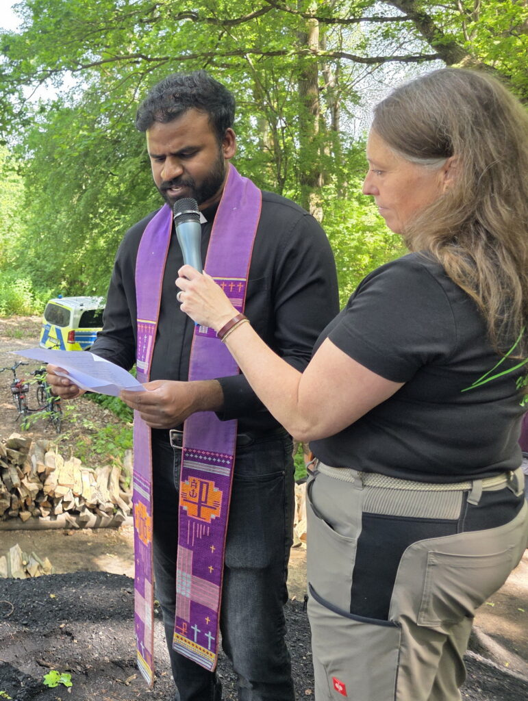 Pfarrer John Bosco sprach auf dem Meilerplatz den Segen über Menschen, Handwerk und Gemeinschaft. Unterstützt wurde er dabei von Moderatorin Sabine Wichmann vom Förderverein Nationalpark Eifel. Foto: Manfred Lang/pp/Agentur ProfiPress