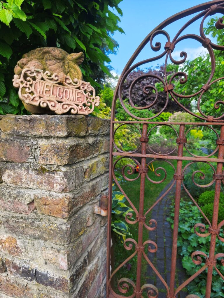 Rostiges Schmiedeeisen trifft altes Mauerwerk. Durch das schnörkelige Gartentörchen fällt der Blick auf einen sanft geschwungenen Pfad. Foto: Kerstin Rottland/pp/Agentur ProfiPress