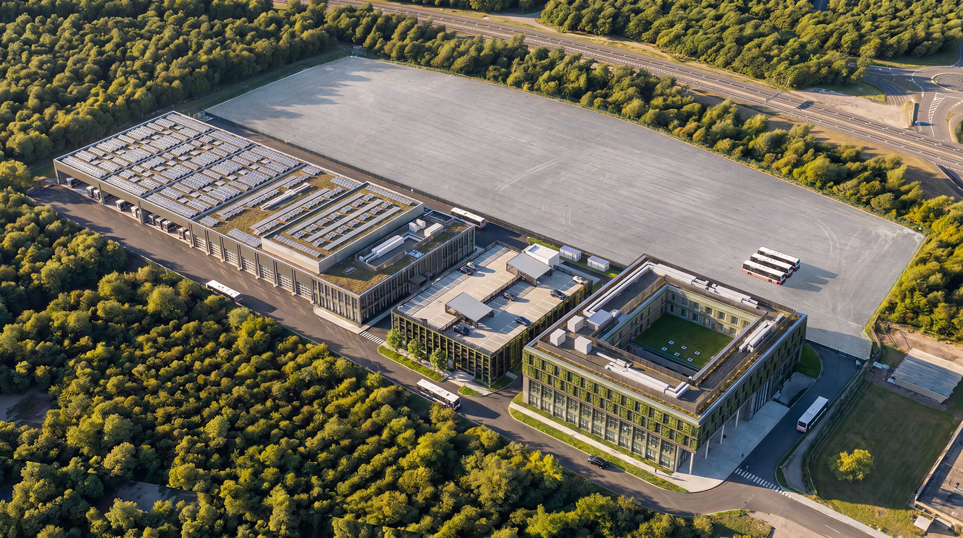 Blick auf die Fahrsicherheitsfläche (oben) sowie auf das Ensemble mit Akademie (v.r.), Parkdeck, Kompetenzzentrum mit angrenzender Werkstatt und Fahrzeughallen mit Platz für 51 Busse. Bild: agn Architekten/pp/Agentur ProfiPress