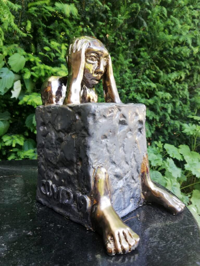 Keramikkunst aus der Stimmung heraus: Liane Bause gestaltete während der Coronapandemie eine menschliche Figur mit resigniertem Gesichtsausdruck, die bewegungslos in einen Metallklotz festgegossen sitzt. Foto: Bause/pp/Agentur ProfiPress