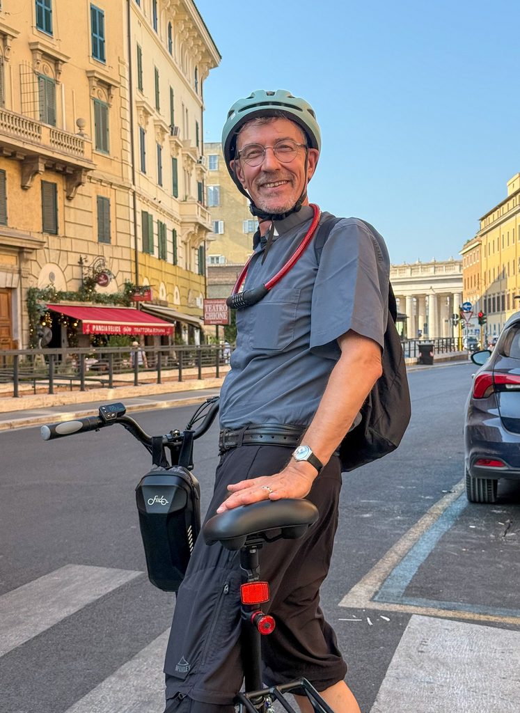 Mit dem E-Bike zur Papstbasilika: Ludwig Kröger braucht von seiner römischen Wohnung nur wenige Minuten bis zu seinem Arbeitsplatz im Petersdom. Hier ist er auf der Via delle Fornaci zu sehen, Berninis Kolonaden im Hintergrund. Foto: © KNA/Sabine Kleyboldt