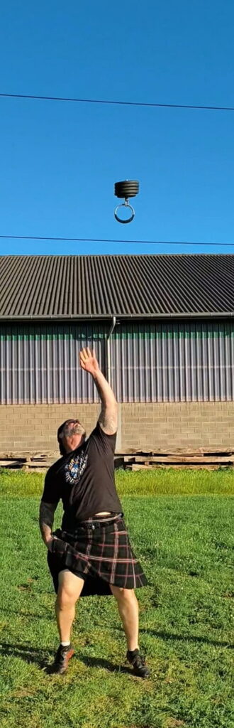 Das Bild zeigt Max „Mäx“ Althoff aus Düren in einem traditionellen Tartan-Kilt und schwarzem T-Shirt, der beim Highland-Game-Training auf dem Hosteler Bolzplatz eine Disziplin im Gewichtwerfen ausübt. Foto: privat/pp/Agentur ProfiPress